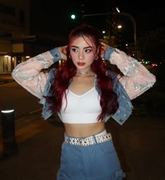 a woman with red hair wearing a white crop top and blue denim skirt standing in the street at night