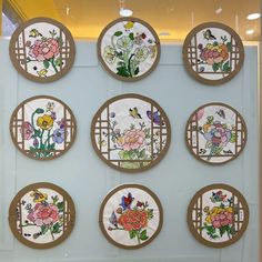 nine plates with flowers painted on them are displayed in a glass display case against a wall