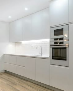 a kitchen with white cabinets and an oven in the center, along with hardwood flooring