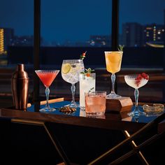 various cocktails are lined up on a table in front of a window at night