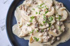 a blue plate topped with ravioli covered in meat and cheese sauce on top of a marble table