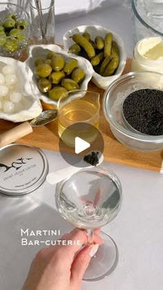 a person is holding a wine glass in front of some olives and other ingredients