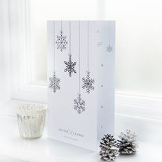 a white card with snowflakes hanging from it next to a cup and pine cones