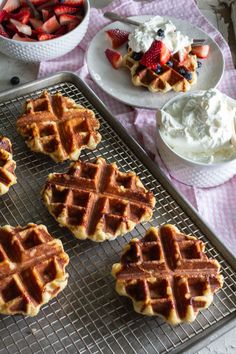 several waffles on a cooling rack with strawberries and whipped cream in the background