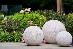 two cement balls sitting on top of a sidewalk next to bushes and flowers in the background