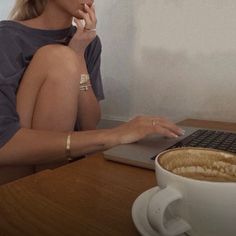 a woman sitting in front of a laptop computer with a cup of coffee on the table