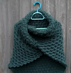 a green crocheted scarf hanging on a wooden wall next to a blue hanger