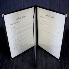 an opened menu is shown on a black tablecloth with gold trimmings and metal handles