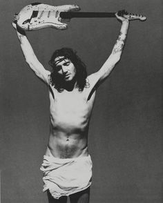 a shirtless man holding an electric guitar above his head