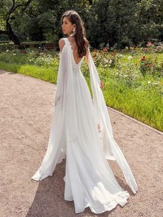 a woman in a white wedding dress is standing on a path with her back to the camera