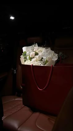 a red bag filled with white flowers sitting on top of a leather seat in the back of a car