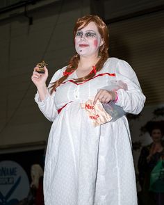 a woman dressed as a zombie holding a piece of food in her hand while standing on stage