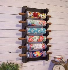 a wall mounted shelf with several rolls of fabric hanging on it's sides and a clock next to it