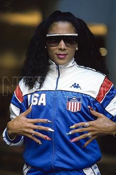 a woman with her hands on her hips wearing an american flag track suit and sunglasses