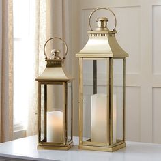 two gold lanterns sitting next to each other on a window sill with curtains in the background