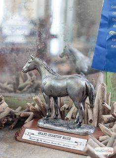 there is a statue of a horse on display in front of a window with driftwood behind it