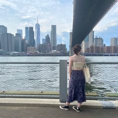 a woman standing on the side of a bridge looking at the water and skyscrapers