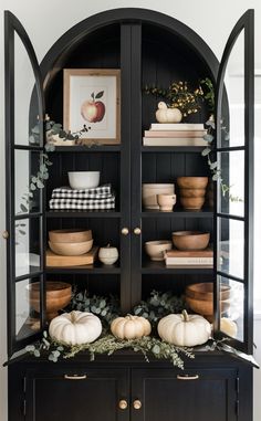 a black china cabinet with white pumpkins and greenery