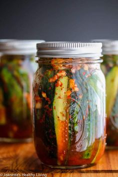 three jars filled with pickles and vegetables on top of a wooden table next to each other