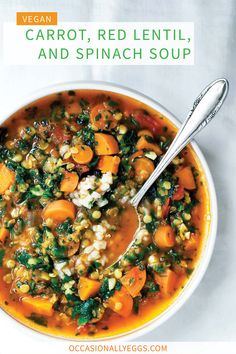 a white bowl filled with carrots, lentil and spinach soup next to a spoon