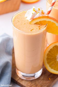 two glasses filled with orange juice and topped with whipped cream next to sliced oranges