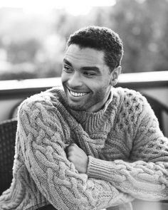 a black and white photo of a man wearing a sweater smiling at the camera with his arms crossed