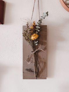 a wooden plaque with dried flowers hanging from it's side on a wall next to a clock