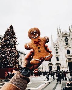 a person is holding up a gingerbread in front of a christmas tree and cathedral