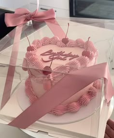 a pink birthday cake in a clear box with ribbon around it and the word happy on top