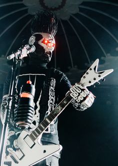 a man with an electric guitar standing in front of a microphone and wearing a mask