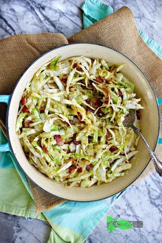 a bowl filled with coleslaw and bacon on top of a blue towel next to a spoon