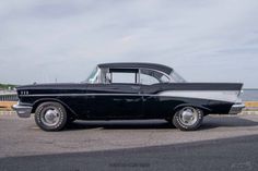 an old black and white car is parked by the water