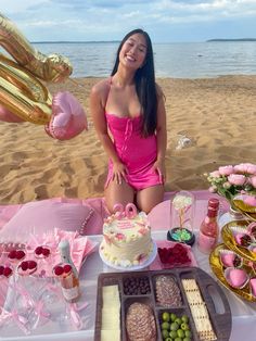 a woman in a pink bathing suit sitting at a table with cake and desserts