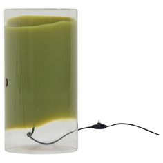 a glass vase with yellow and green liquid in it next to a black cord that is plugged into the wall