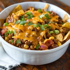 a white bowl filled with chili cheese and tortilla chips on top of a wooden table