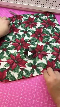 someone cutting fabric with scissors on a pink mat in the shape of poinsettis