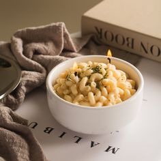 a white bowl filled with macaroni and cheese on top of a table next to a book