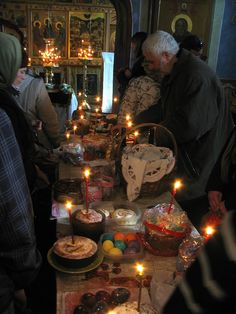 many people are gathered around a table with candles on it and food in front of them