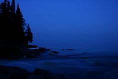 the moon is shining over some trees and rocks in the dark blue night time sky