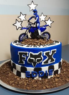 a blue and white cake with a dirt bike on it's bottom tier is decorated with stars