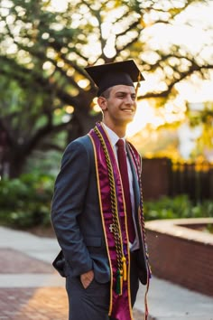 a man in a graduation gown and cap is standing on the sidewalk with his hands in his pockets