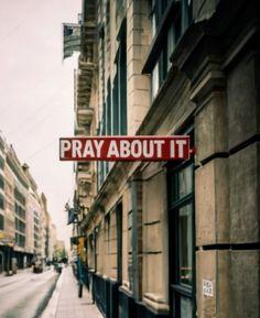 a red sign that says pray about it hanging from the side of a building on a city street