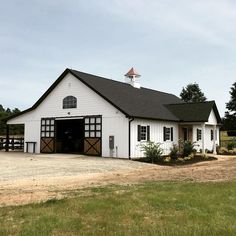 a large white barn with a black roof and two doors on the side of it