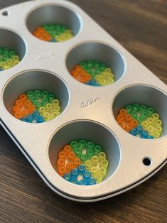 a muffin tin filled with lots of colorful beads on top of a wooden table