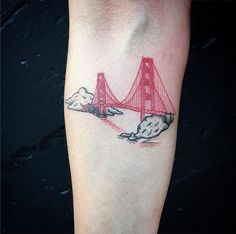 a red bridge tattoo on the left arm with clouds and mountains in front of it