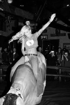 a woman riding on the back of a brown and white cow in front of a crowd