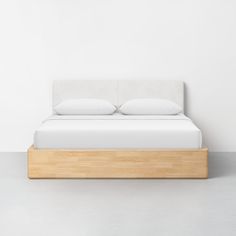 a bed with white sheets and pillows on top of it, sitting in front of a wall