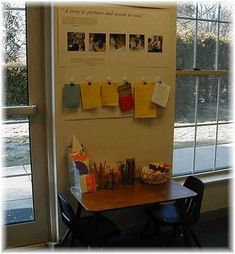 there is a table and chairs in front of a bulletin board with pictures on it