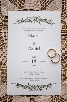 two wedding rings are placed on top of a white card with greenery in the background