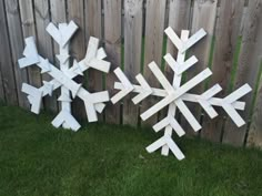 two snowflakes made out of wood sitting in the grass next to a fence